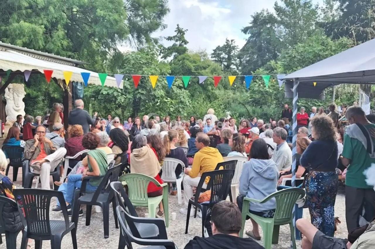 Un groupe de personnes assises en extérieur, participant à un événement sous des guirlandes de fanions colorés.