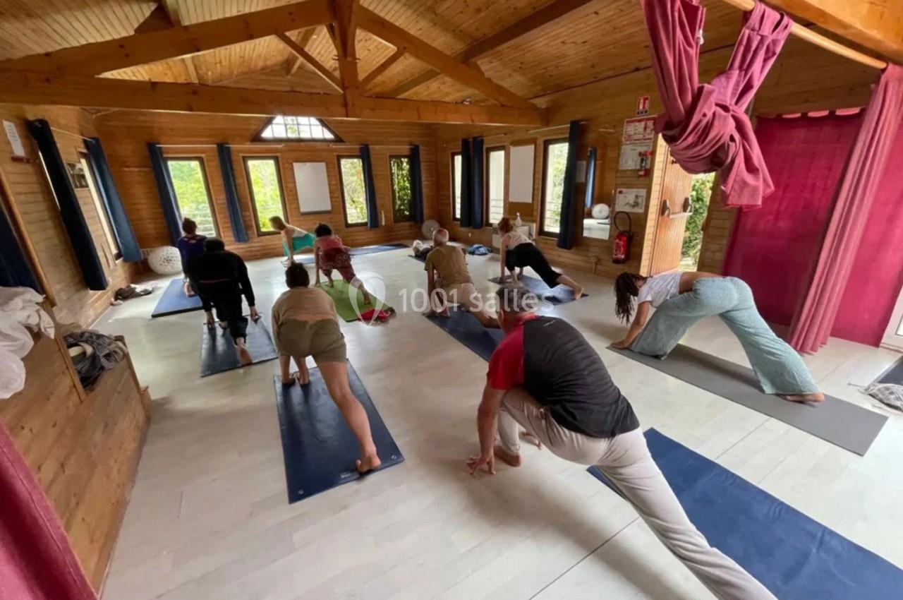 Personnes pratiquant le yoga dans une salle en bois lumineuse, chacune sur un tapis, en position d'étirement.