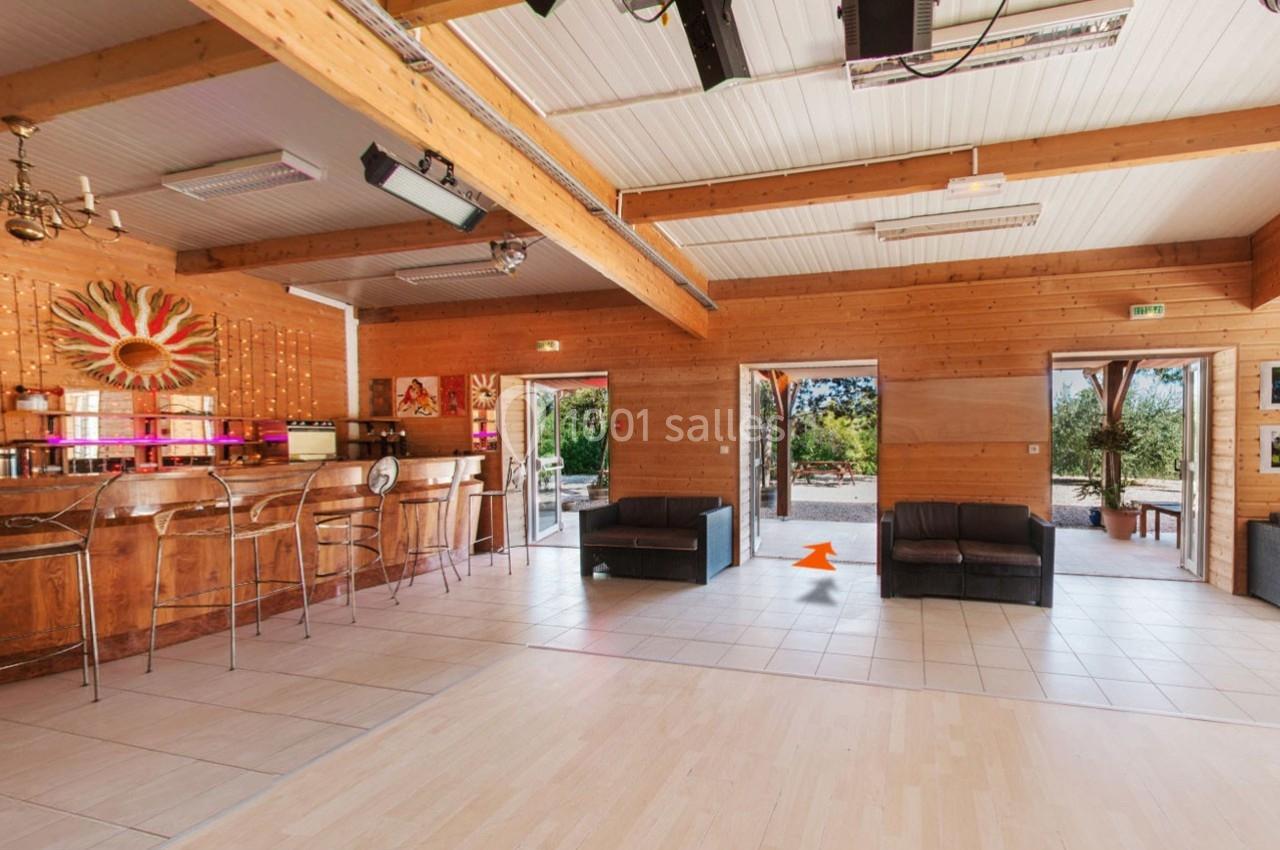 Intérieur d'une salle lumineuse avec bar en bois, canapés, décorations murales et ouvertures donnant sur un jardin.