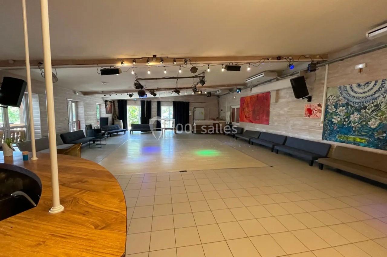 Salle spacieuse avec sol carrelé, banquettes le long des murs, bar en bois et décorations murales colorées.