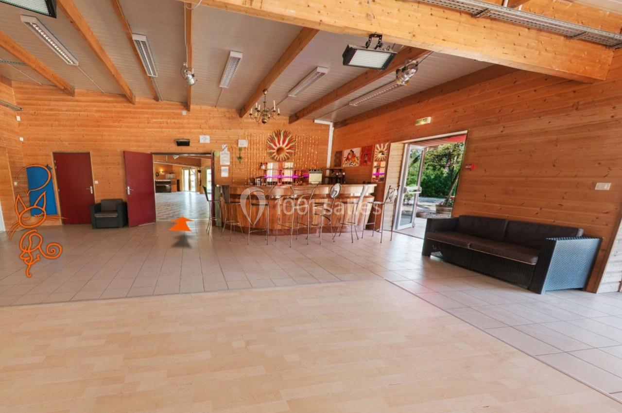 Salle en bois avec un bar central, des chaises hautes, un canapé, et une porte ouverte donnant sur l'extérieur.