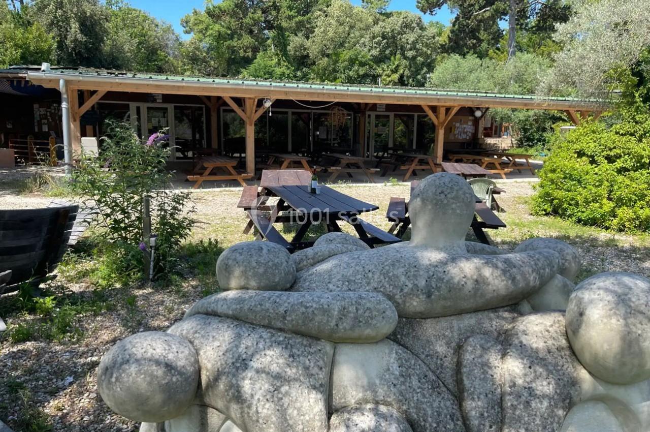Sculpture en pierre représentant des figures humaines enlacées, avec des tables de pique-nique et un bâtiment en arrière…