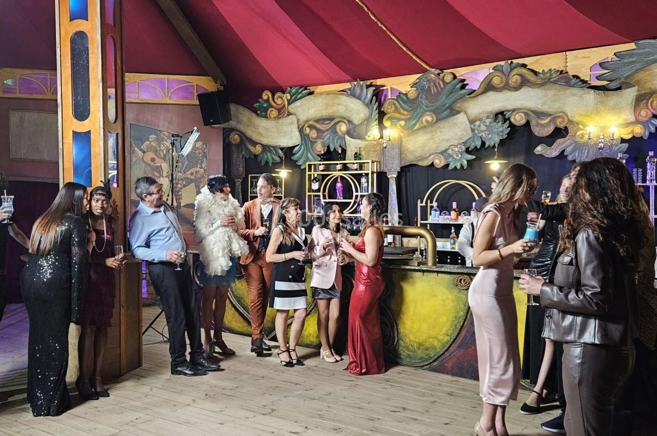 Des personnes élégamment habillées discutent et boivent dans un bar à la décoration colorée et théâtrale.