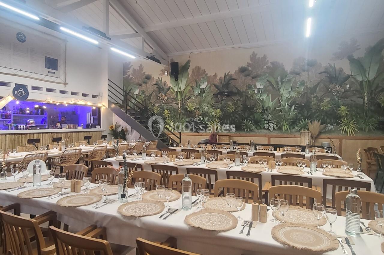 Salle de réception décorée avec des tables dressées, chaises en bois et fresque murale représentant une jungle tropicale.