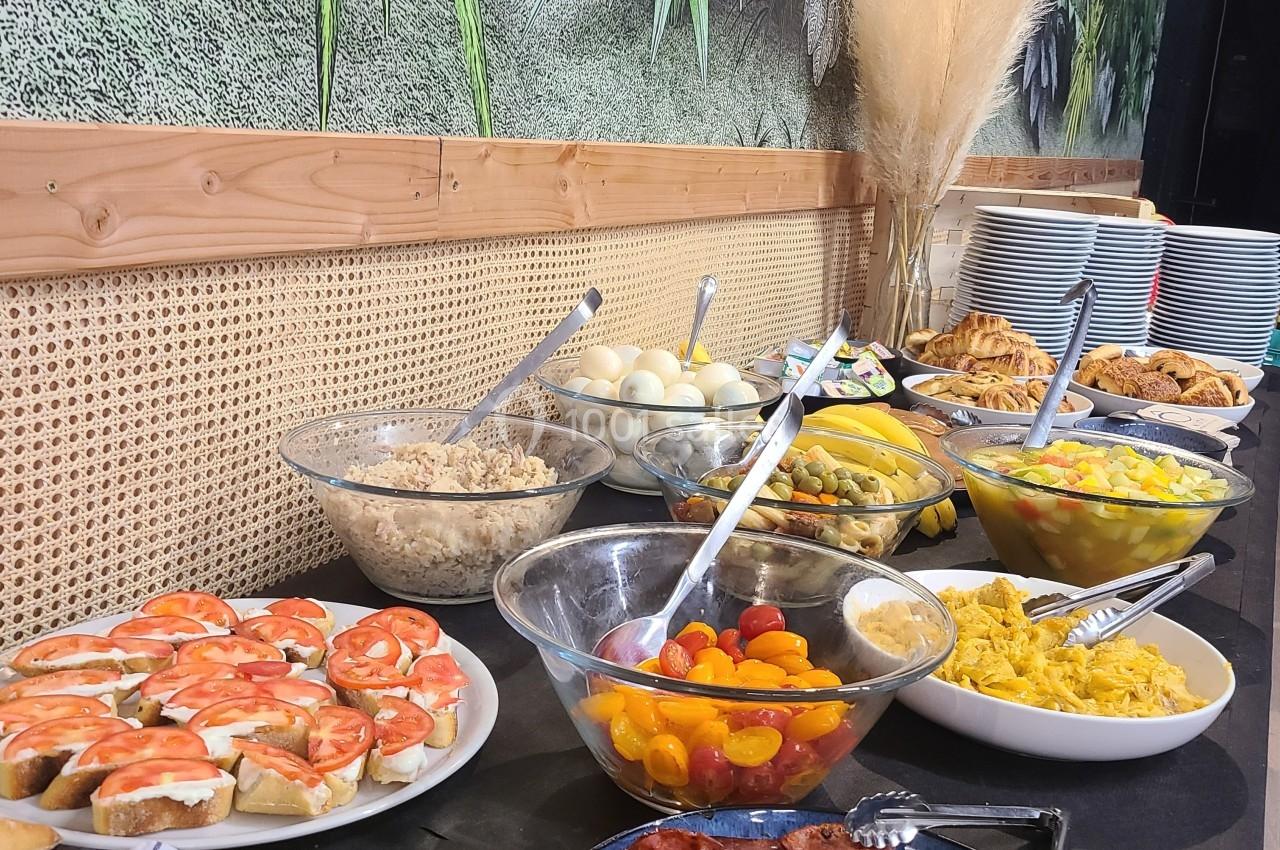 Buffet varié avec charcuterie, légumes, œufs, pains et salades, disposé sur une table devant un mur végétalisé.