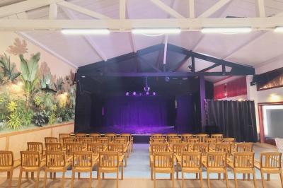 Salle lumineuse avec tables blanches disposées en U, chaises en bois et murs clairs dans un espace modulaire.