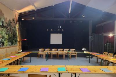 Salle lumineuse avec tables blanches disposées en U, chaises en bois et murs clairs dans un espace modulaire.