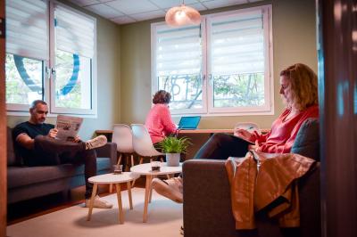 Bureau partagé avec plantes, carte posée sur un support en bois, et personnes travaillant en arrière-plan.