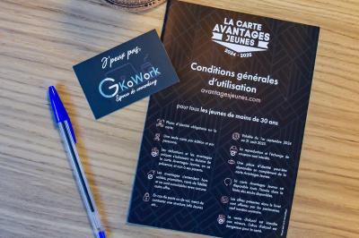 Bureau partagé avec plantes, carte posée sur un support en bois, et personnes travaillant en arrière-plan.