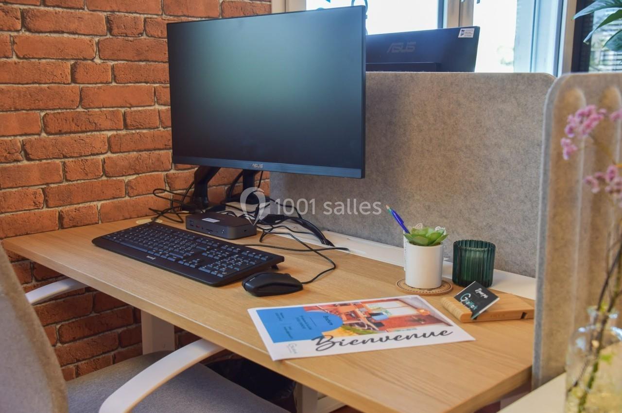 Bureau avec écran d'ordinateur, clavier, souris, plante, bougie et documents posés sur une table en bois clair.