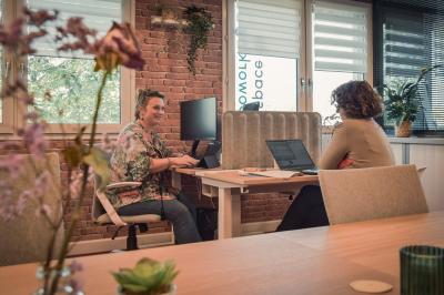 Bureau partagé avec plantes, carte posée sur un support en bois, et personnes travaillant en arrière-plan.