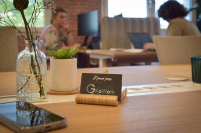 Bureau partagé avec plantes, carte posée sur un support en bois, et personnes travaillant en arrière-plan.