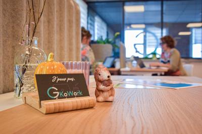 Bureau partagé avec plantes, carte posée sur un support en bois, et personnes travaillant en arrière-plan.