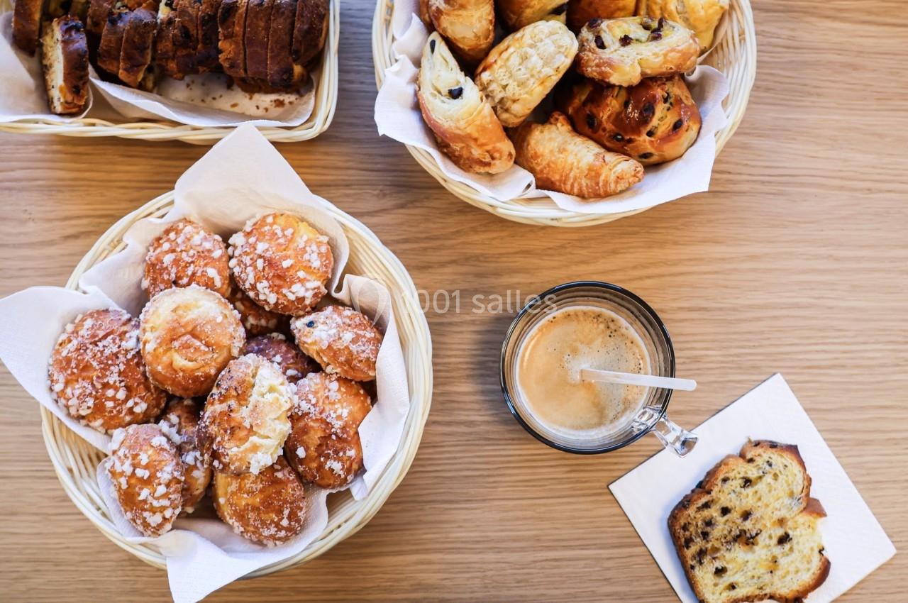 Assortiment de viennoiseries et de pain dans des paniers, accompagné d'une tasse de café sur une table en bois.