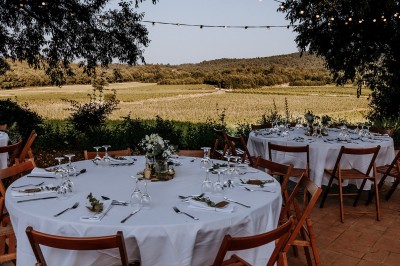 Un couple en tenue de mariage marche main dans la main dans un vignoble, la mariée levant un bouquet.