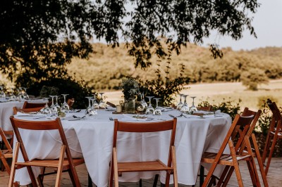 Un couple en tenue de mariage marche main dans la main dans un vignoble, la mariée levant un bouquet.
