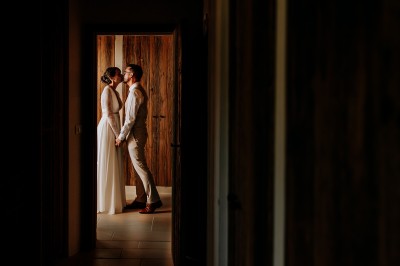 Un couple en tenue de mariage marche main dans la main dans un vignoble, la mariée levant un bouquet.