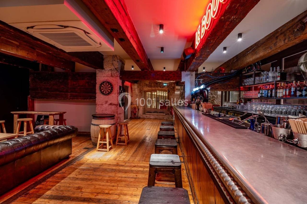 Intérieur d'un bar avec comptoir en bois, tabourets, canapé en cuir, éclairage néon et décoration rustique.