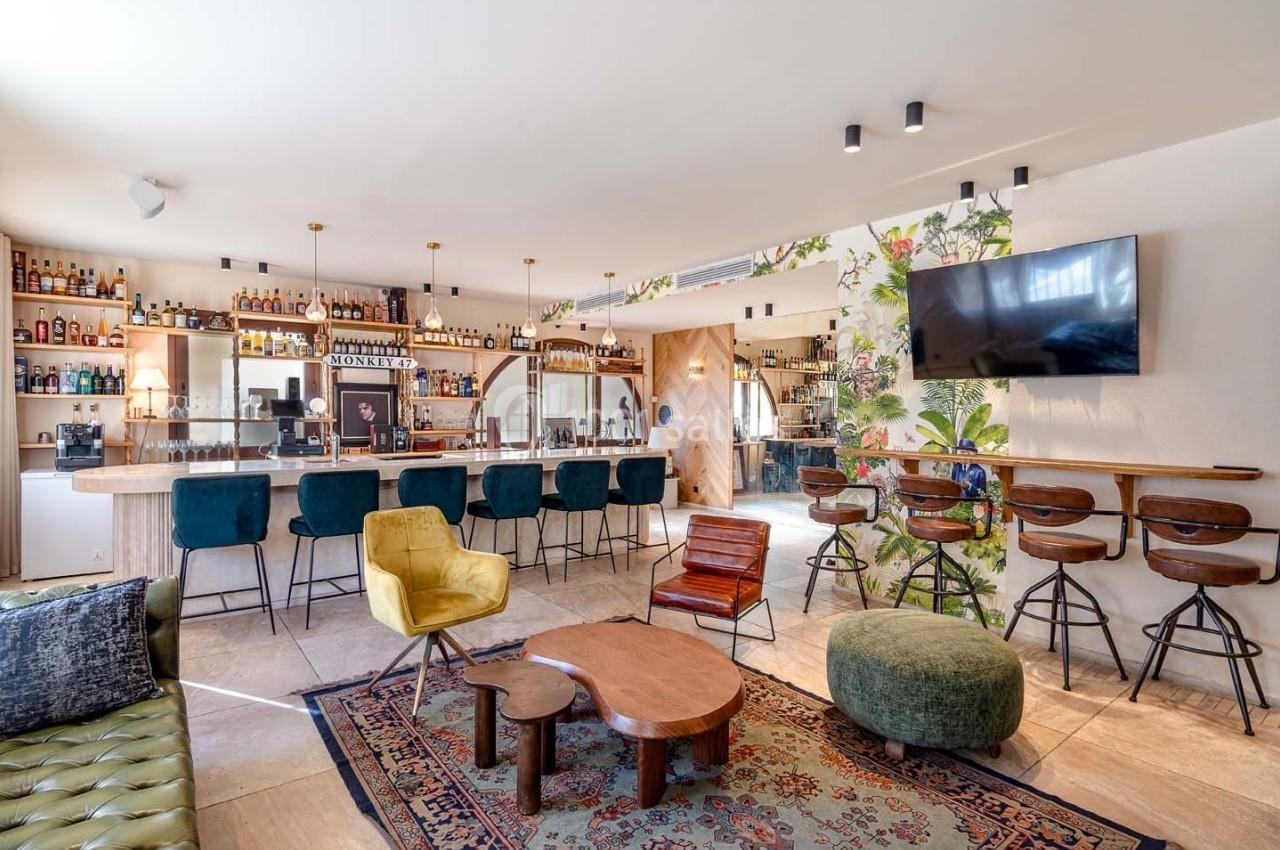 Intérieur d'un bar moderne avec comptoir, tabourets, fauteuils colorés, tapis et décoration murale florale.