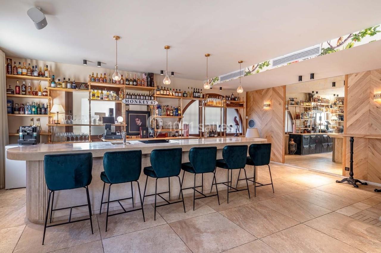 Bar moderne avec comptoir en marbre, tabourets verts, étagères remplies de bouteilles et éclairage chaleureux.