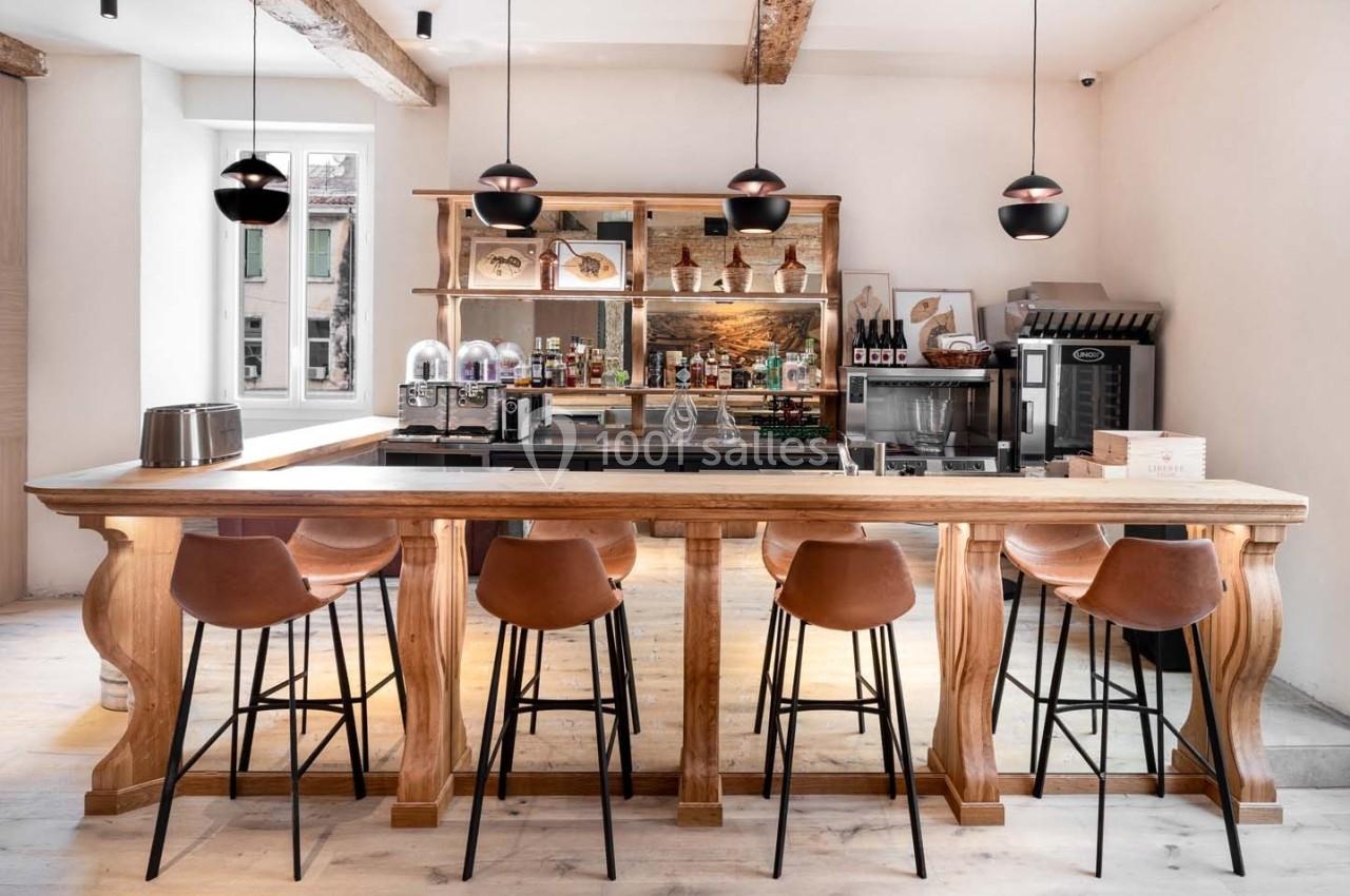Bar en bois clair avec tabourets en cuir, éclairé par des suspensions noires, dans un intérieur lumineux et épuré.