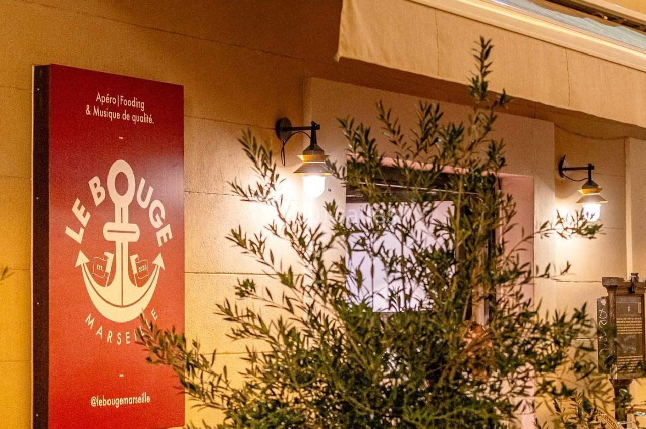 Façade d'un établissement avec une enseigne rouge affichant ’Le Bouge Marseille’, éclairée par des lampes murales.