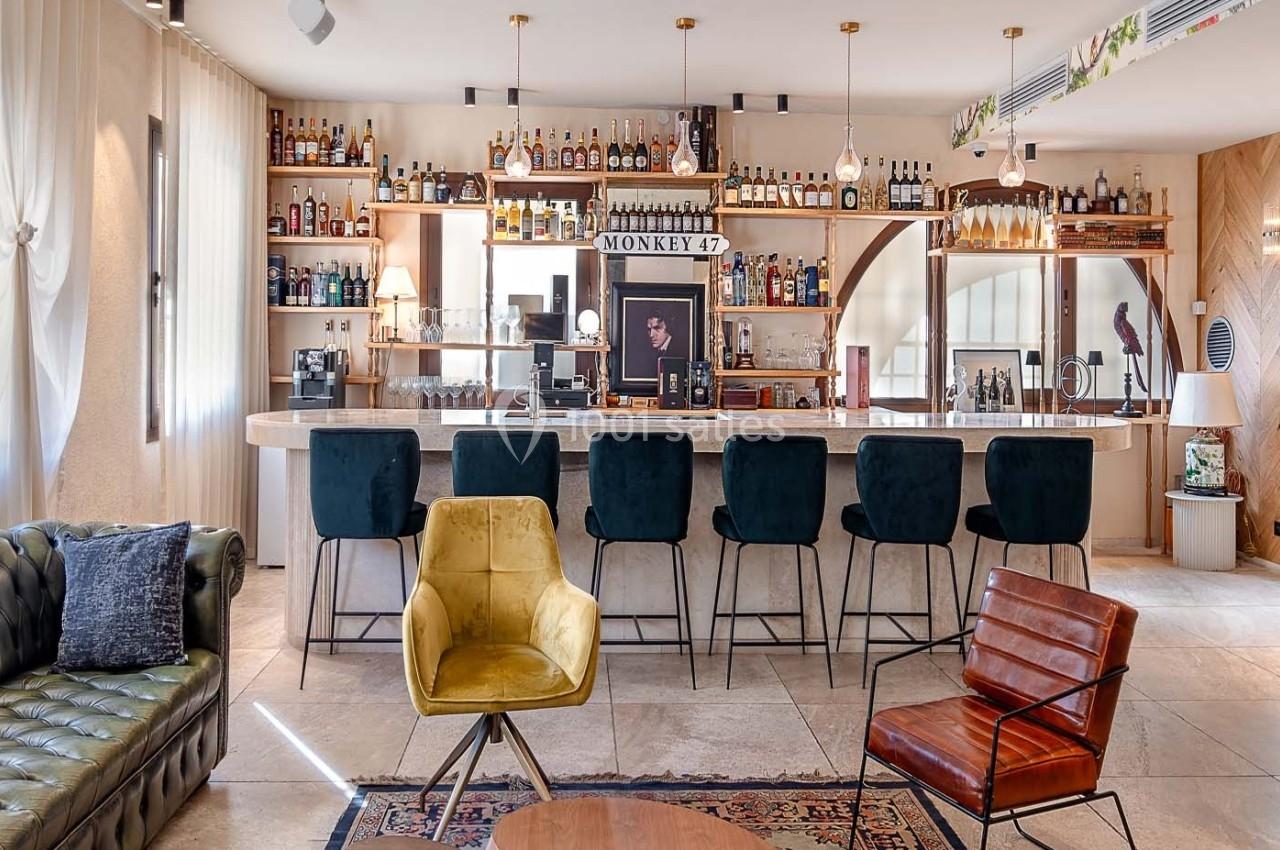 Bar élégant avec comptoir en bois, tabourets noirs, étagères remplies de bouteilles et fauteuils confortables au premier…