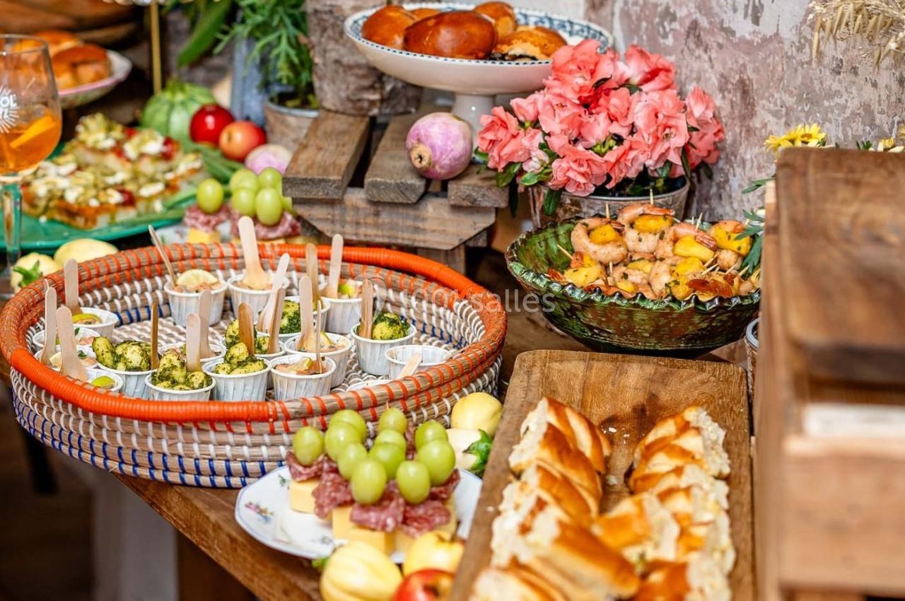 Buffet varié avec plats salés, fruits, brochettes, viennoiseries et fleurs décoratives en arrière-plan.