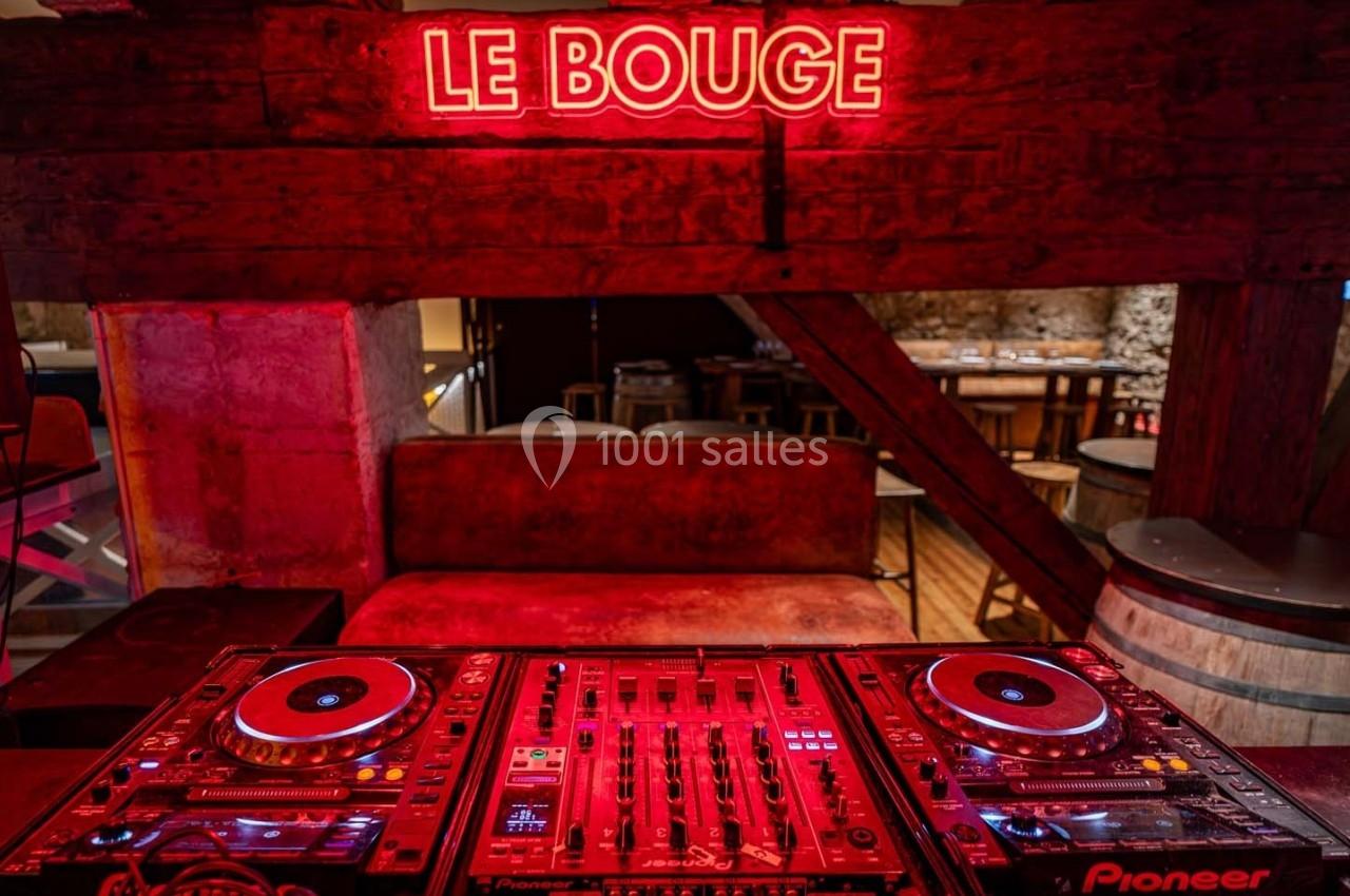 Table de mixage avec platines sous un néon rouge ’Le Bouge’ dans un décor intérieur rustique avec murs en pierre.