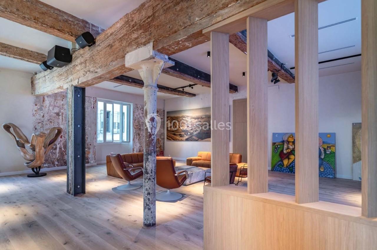 Espace intérieur lumineux avec poutres apparentes, mobilier moderne et œuvres d'art exposées sur les murs.