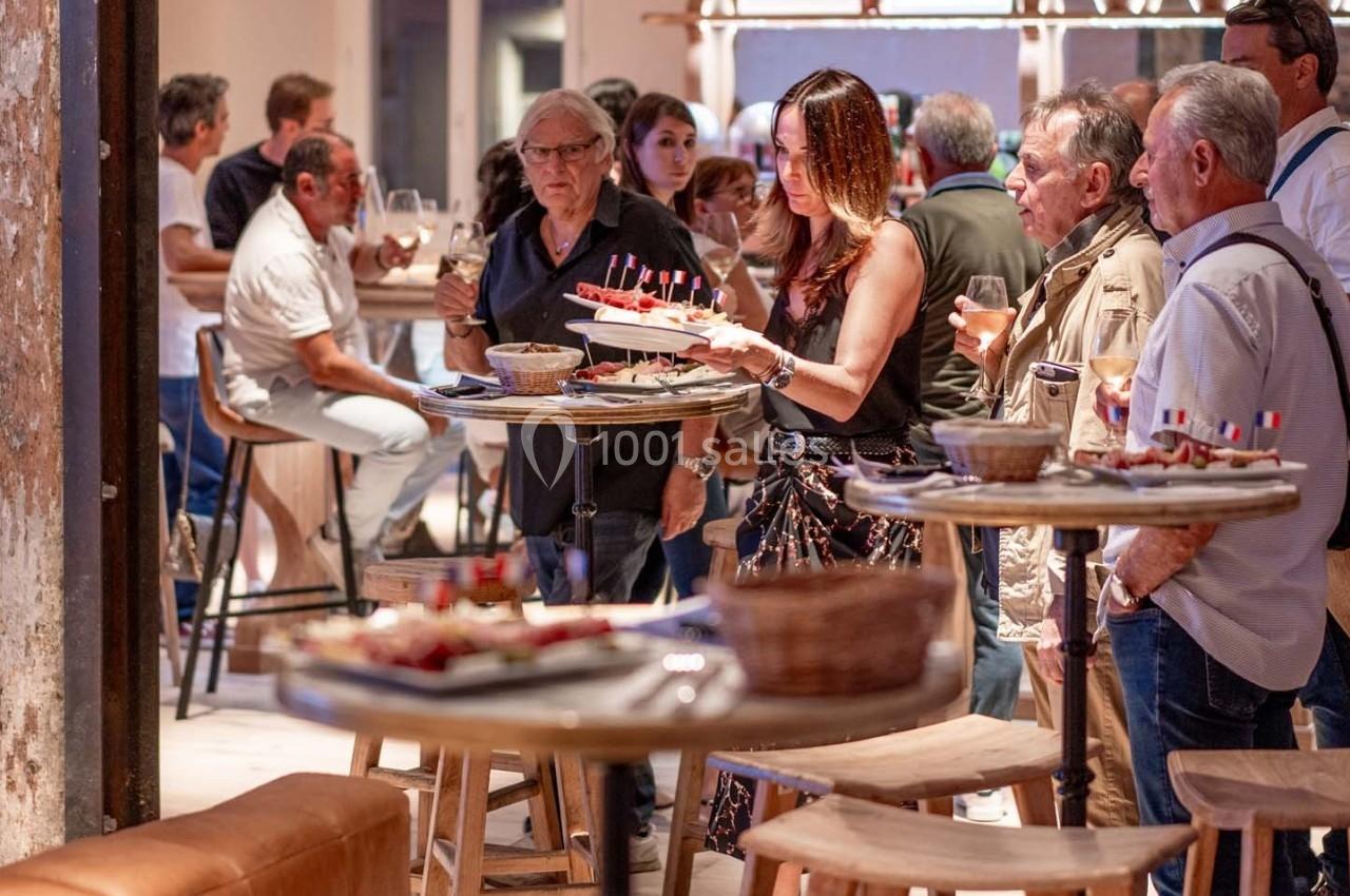 Des personnes discutent et dégustent des amuse-bouches dans un espace convivial avec des tables hautes en bois.