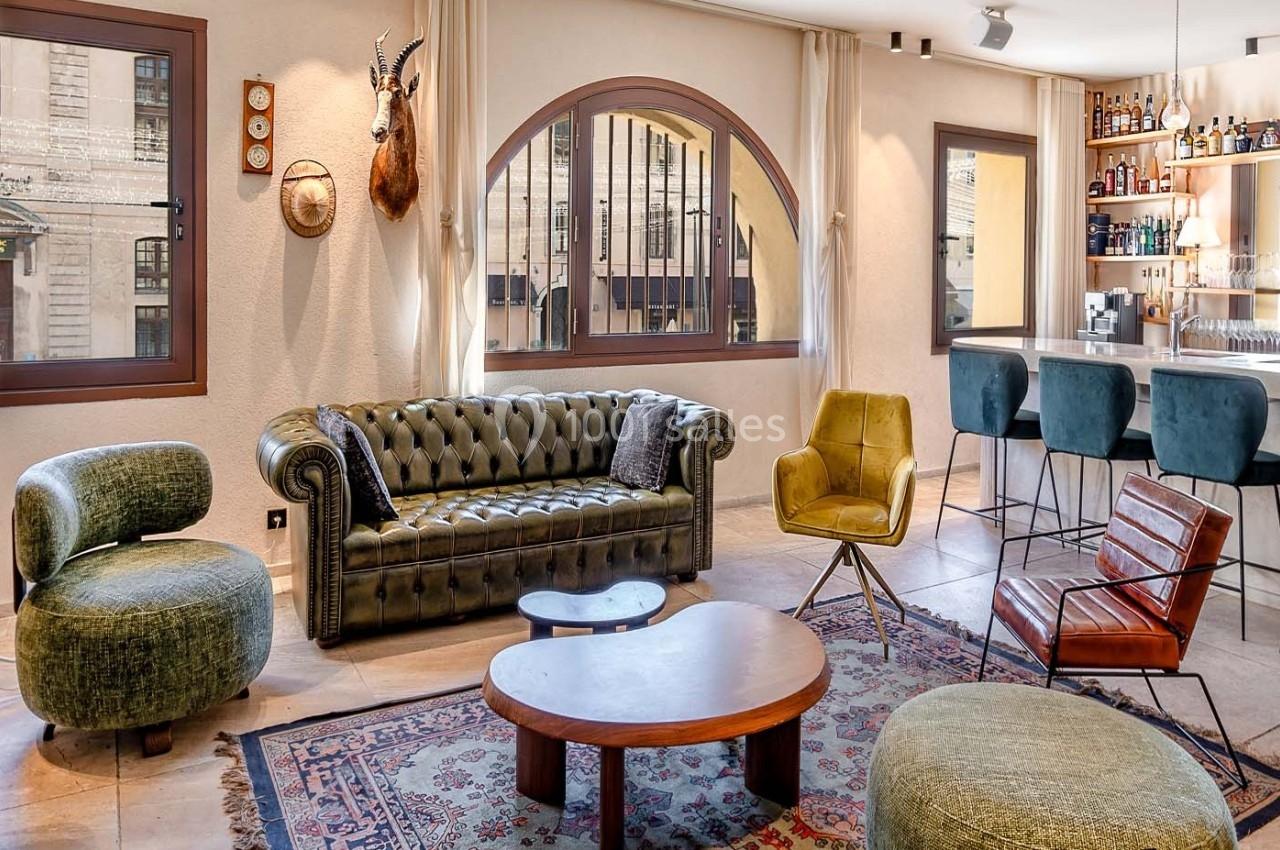 Salon lumineux avec canapé en cuir vert, fauteuils design, tables basses en bois, bar et décorations murales.