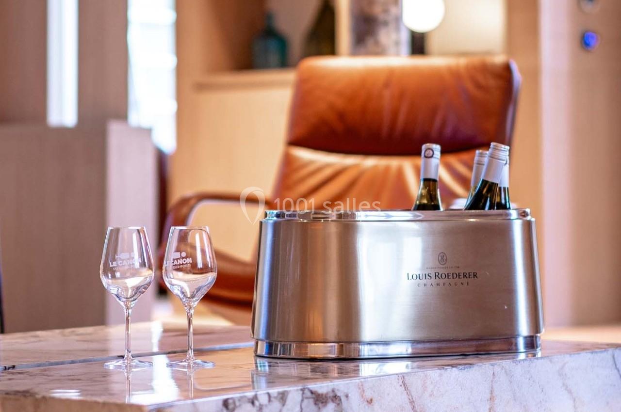 Seau à champagne avec bouteilles et deux verres sur une table en marbre, fauteuil en cuir en arrière-plan.