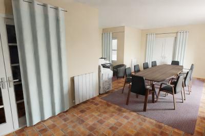 Salle de réunion avec grande table en bois, chaises noires, cheminée allumée et sol en carrelage.
