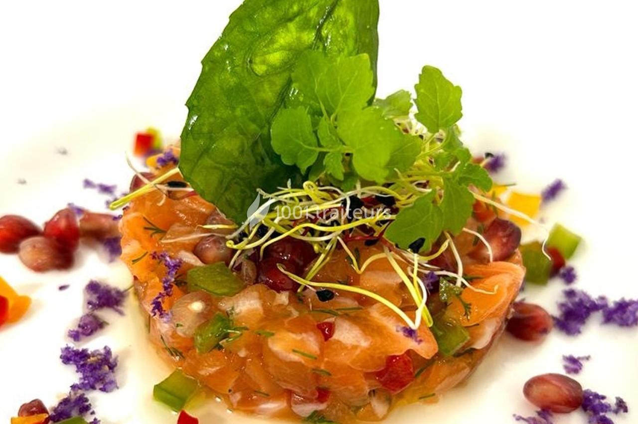 Tartare de saumon garni de jeunes pousses, grenade, herbes fraîches et légumes colorés, présenté sur une assiette blanche.
