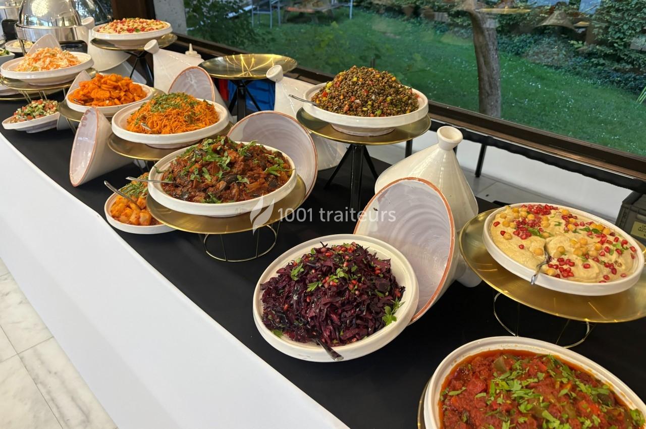 Buffet de plats variés comprenant salades, légumes et mezzés, présenté sur des supports dorés dans un cadre lumineux.