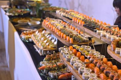 Plateaux garnis de sushis variés, alignés sur une table pour un buffet, avec des sauces en arrière-plan.