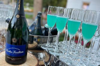 Bouteille de champagne et flûtes remplies d'un cocktail bleu, disposées sur une table en extérieur.