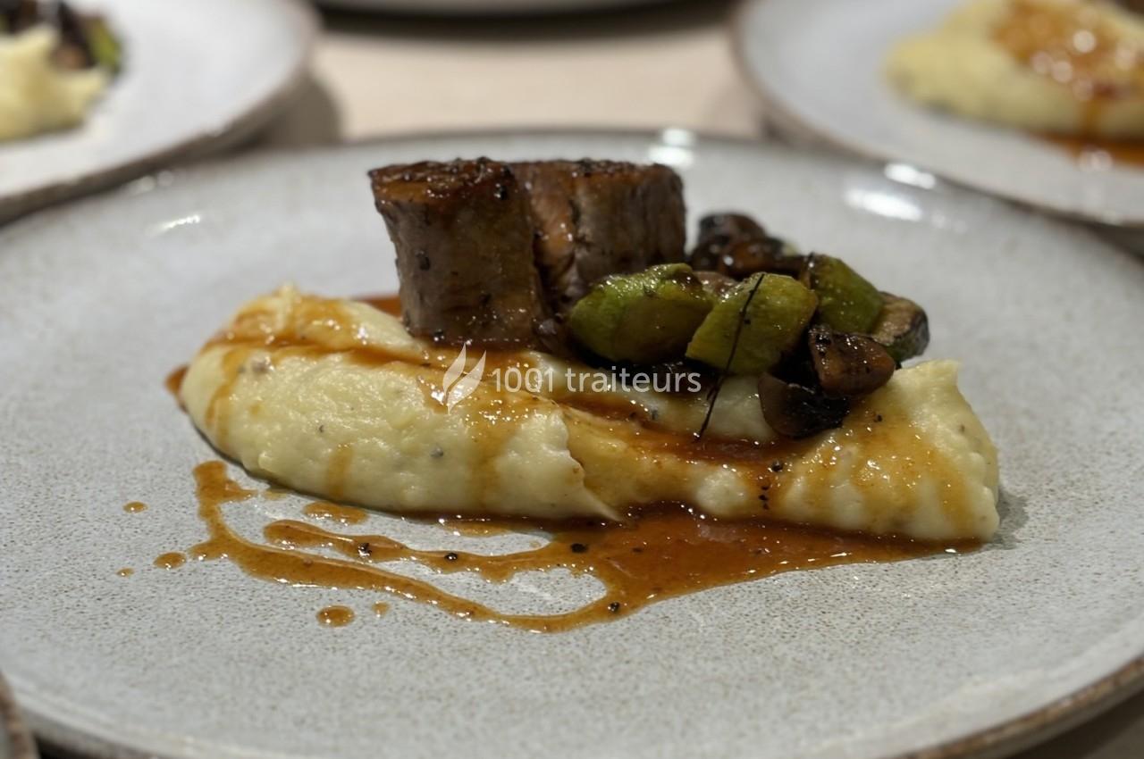 Assiette contenant une purée crémeuse garnie de viande, légumes verts et champignons avec une sauce.