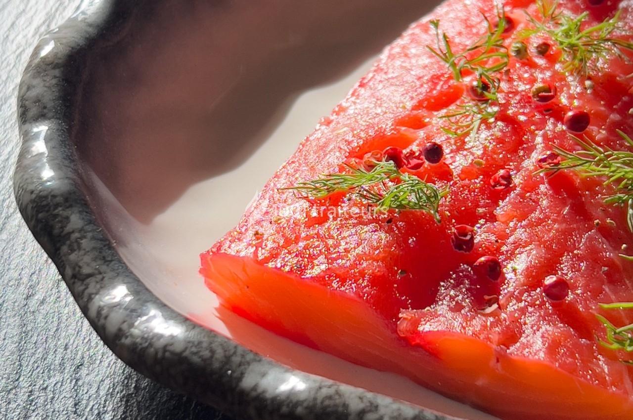Tranche de saumon mariné, garnie d'aneth et de baies roses, servie dans une assiette en céramique.