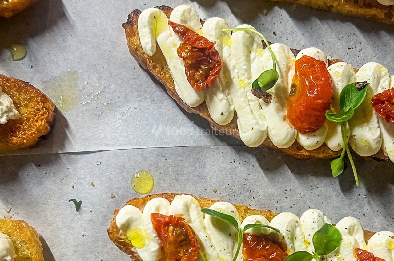 Tranches de pain grillé garnies de fromage frais, tomates confites et micro-pousses, disposées sur du papier cuisson.