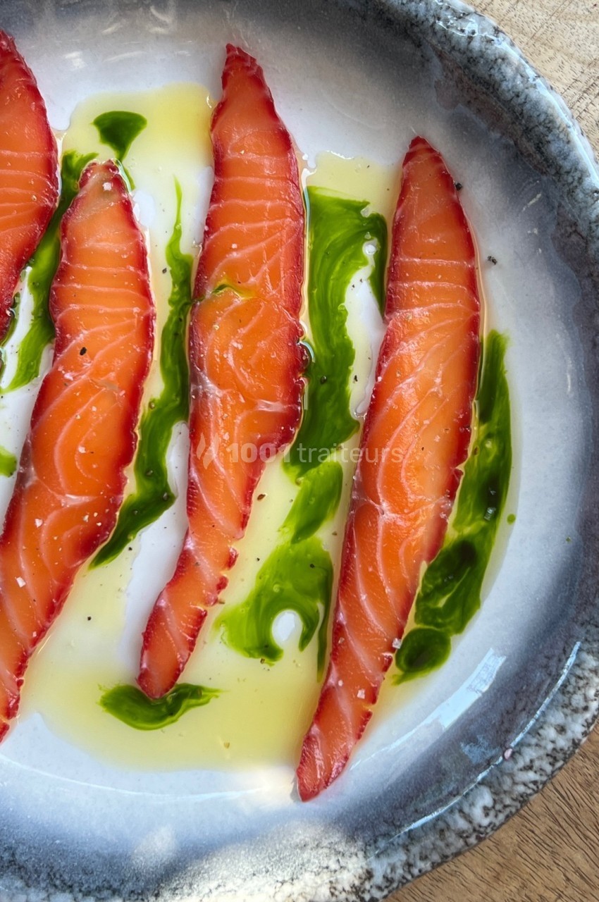 Tranches de saumon cru marinées, disposées sur une assiette avec de l'huile et une sauce verte.