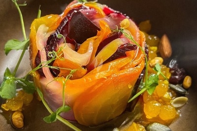 Un chef en tablier marron sourit, bras croisés, dans une cuisine moderne lumineuse.