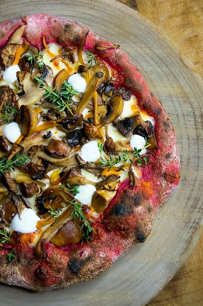 Pizza garnie de champignons, fromage fondu, herbes fraîches et touches de crème, servie sur une planche en bois.