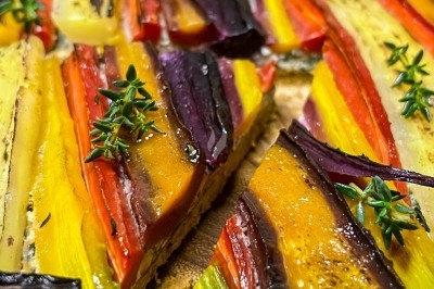 Un chef en tablier marron sourit, bras croisés, dans une cuisine moderne lumineuse.
