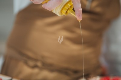 Un chef en tablier marron sourit, bras croisés, dans une cuisine moderne lumineuse.