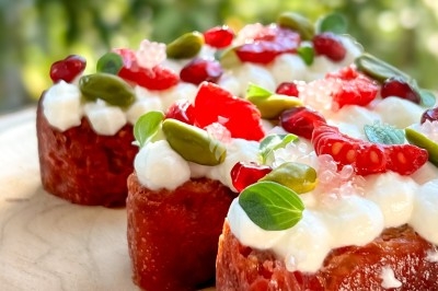 Tranches de brioche garnies de crème, graines, fruits rouges et pistaches, présentées sur une planche en bois.