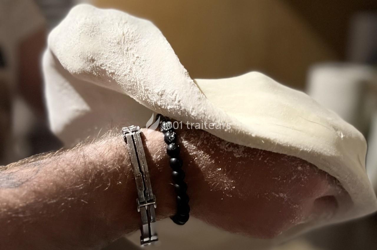 Main tenant une pâte à pizza fine et légèrement farinée, prête à être étirée ou façonnée.