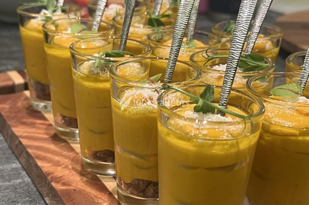 Verrines de velouté orange garnies de feuilles vertes, parmesan râpé et cuillères argentées.