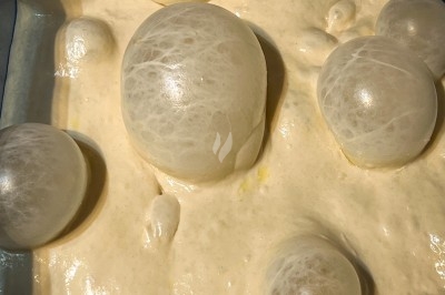 Un chef en tablier marron croise les bras devant un plan de travail dans une cuisine moderne.